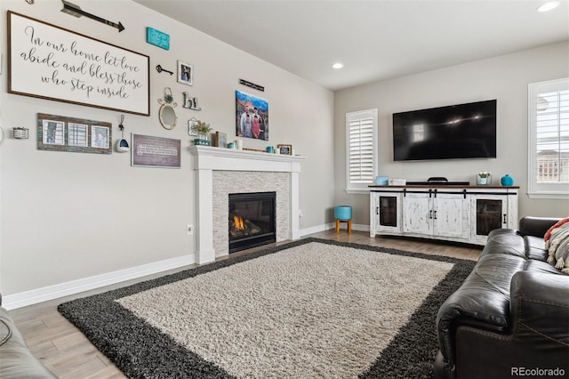 living area featuring baseboards, wood finished floors, recessed lighting, and a stone fireplace