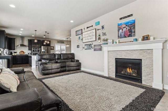 living room featuring light wood-style flooring, a stone fireplace, baseboards, and recessed lighting