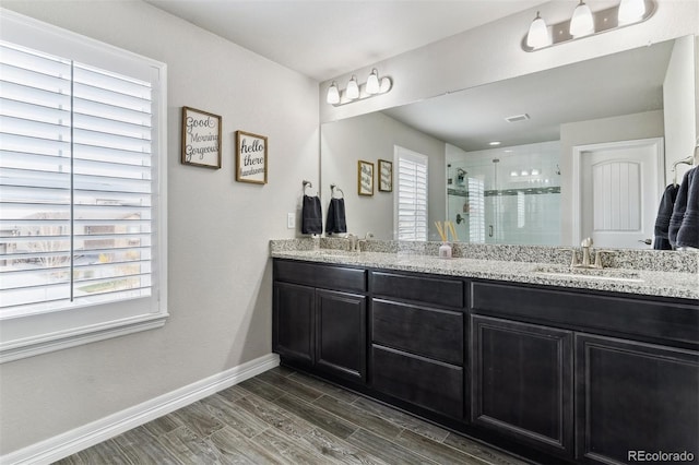 full bath featuring a sink, a shower stall, baseboards, wood tiled floor, and double vanity