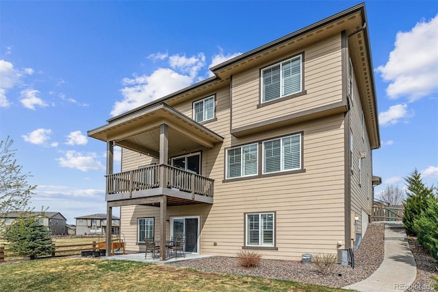 rear view of property with a balcony, fence, a patio, and a lawn