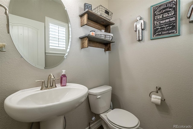 bathroom with toilet, a sink, and a textured wall