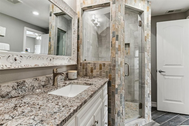 full bathroom featuring visible vents, wood finish floors, a ceiling fan, vanity, and a stall shower