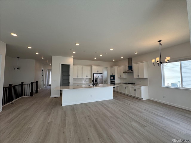 kitchen featuring a center island with sink, stainless steel fridge with ice dispenser, white cabinetry, wall chimney exhaust hood, and a chandelier