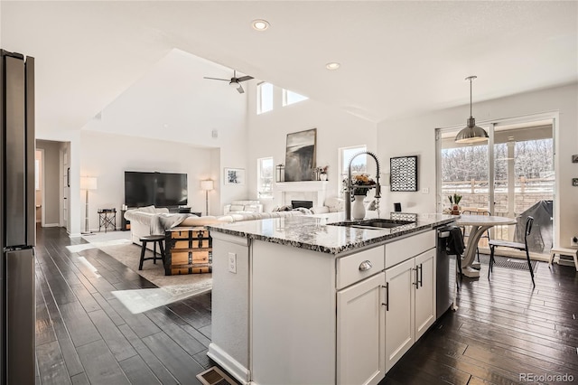 kitchen with decorative light fixtures, stone countertops, open floor plan, white cabinets, and a sink