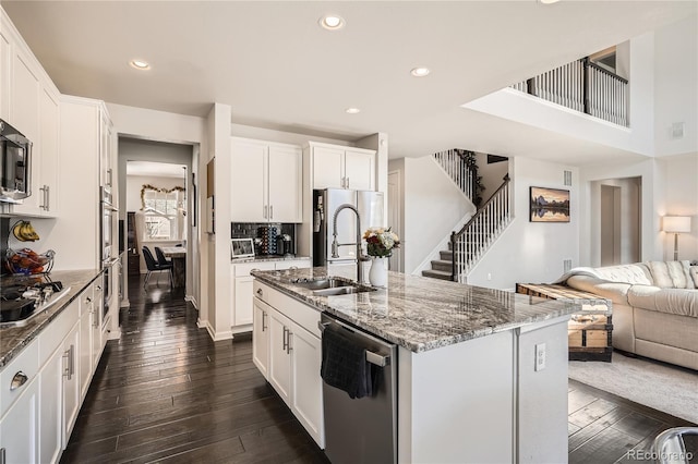 kitchen with open floor plan, stainless steel appliances, a center island with sink, and white cabinetry