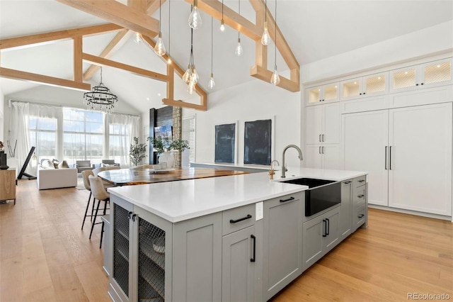 kitchen with sink, hanging light fixtures, light wood-type flooring, gray cabinets, and an island with sink