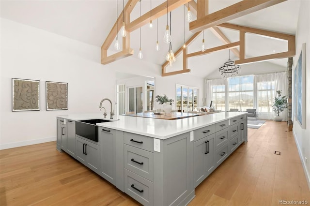 kitchen featuring pendant lighting, sink, gray cabinetry, a kitchen island with sink, and light hardwood / wood-style flooring