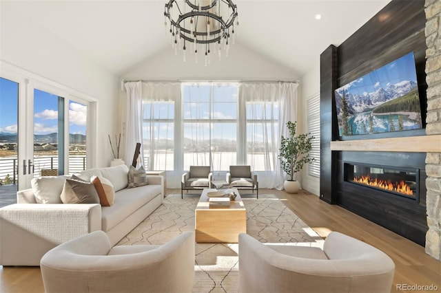 living room featuring light hardwood / wood-style flooring, high vaulted ceiling, a water view, a fireplace, and a chandelier