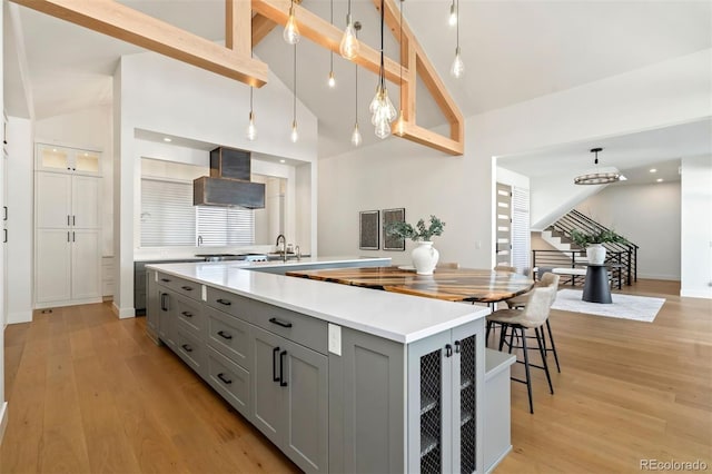 kitchen featuring a spacious island, custom exhaust hood, gray cabinets, pendant lighting, and light hardwood / wood-style floors