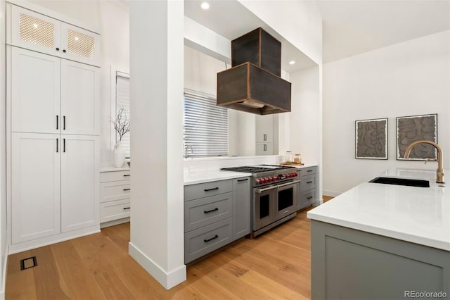 kitchen with double oven range, sink, island range hood, and light wood-type flooring