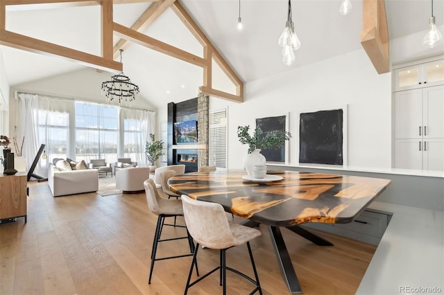 dining room featuring beam ceiling, high vaulted ceiling, a large fireplace, and light wood-type flooring