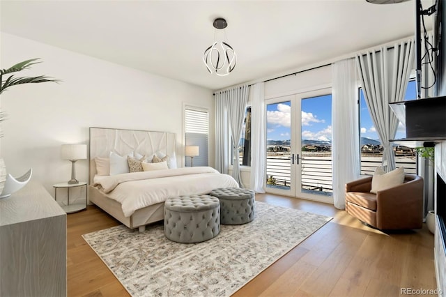 bedroom featuring french doors, an inviting chandelier, hardwood / wood-style floors, and access to outside