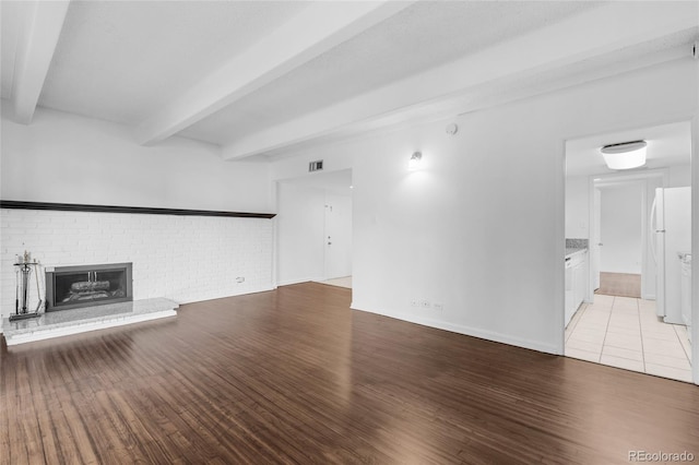 unfurnished living room featuring light hardwood / wood-style floors, beamed ceiling, and a brick fireplace