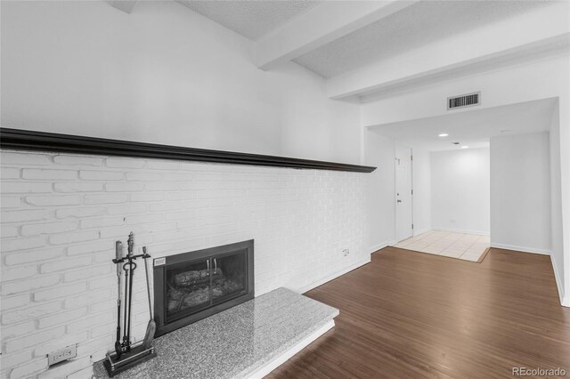 living room featuring a textured ceiling, beam ceiling, wood-type flooring, and a brick fireplace