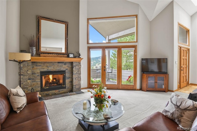 living room with french doors, light colored carpet, a stone fireplace, and high vaulted ceiling