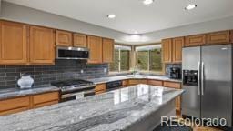 kitchen with appliances with stainless steel finishes, sink, light stone counters, and decorative backsplash