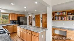 kitchen with stainless steel refrigerator with ice dispenser, light brown cabinetry, a center island, light hardwood / wood-style floors, and backsplash