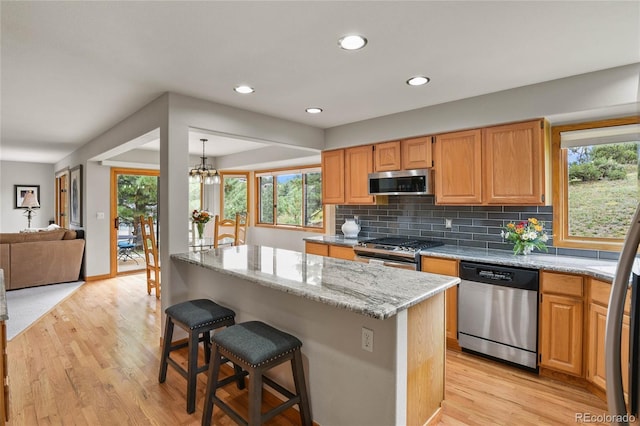 kitchen featuring a breakfast bar area, light stone counters, light hardwood / wood-style flooring, appliances with stainless steel finishes, and pendant lighting