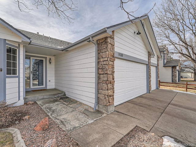 view of side of home featuring a shingled roof, stone siding, driveway, and an attached garage