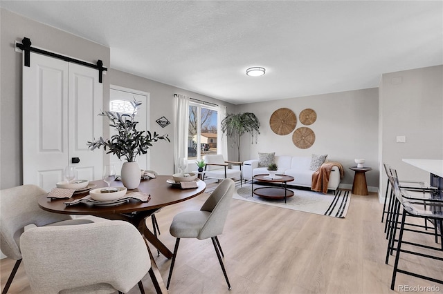 dining area featuring baseboards, light wood-style flooring, a textured ceiling, and a barn door