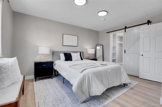 bedroom featuring a barn door, light wood-style flooring, and baseboards