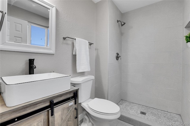 full bathroom featuring vanity, toilet, a textured wall, and a tile shower