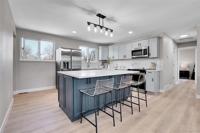 kitchen with light wood-type flooring, stainless steel appliances, backsplash, and visible vents