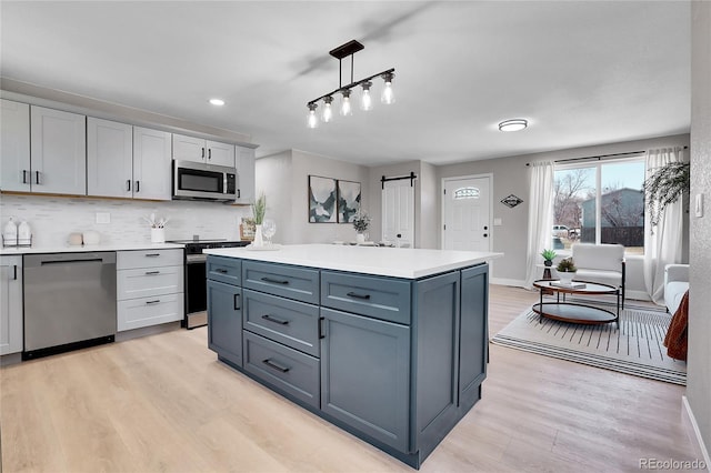 kitchen with light wood-style flooring, light countertops, appliances with stainless steel finishes, a barn door, and backsplash