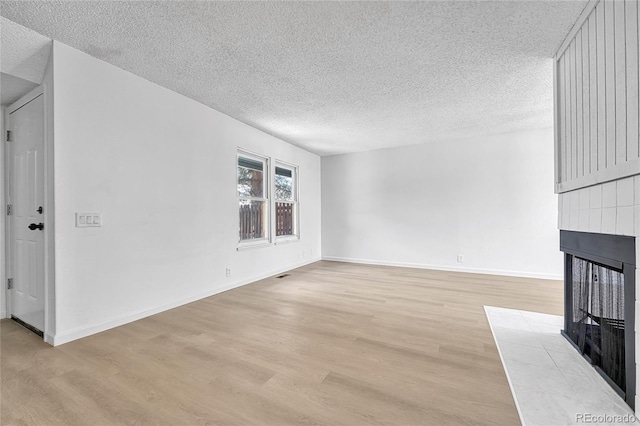 unfurnished living room featuring a tiled fireplace, a textured ceiling, light wood-style floors, and baseboards