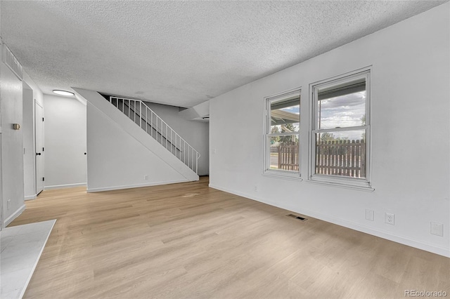 unfurnished living room featuring visible vents, stairs, baseboards, a textured ceiling, and light wood-style flooring