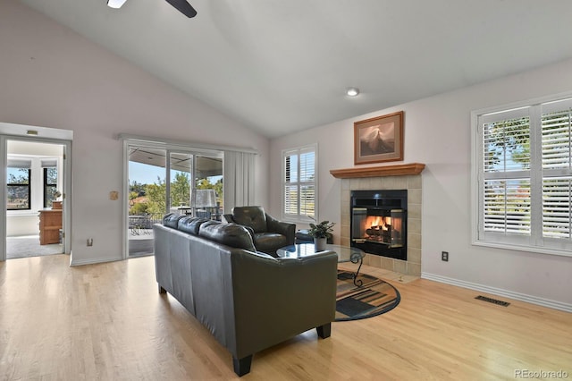 living room with hardwood / wood-style flooring, ceiling fan, vaulted ceiling, and a tiled fireplace