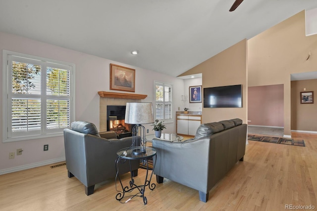 living room with ceiling fan, lofted ceiling, a fireplace, and light hardwood / wood-style flooring