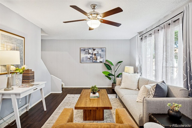 living room with ceiling fan, a textured ceiling, wooden walls, and dark wood-type flooring