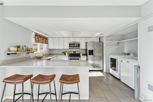 kitchen with white cabinets, kitchen peninsula, a kitchen breakfast bar, appliances with stainless steel finishes, and washer and dryer