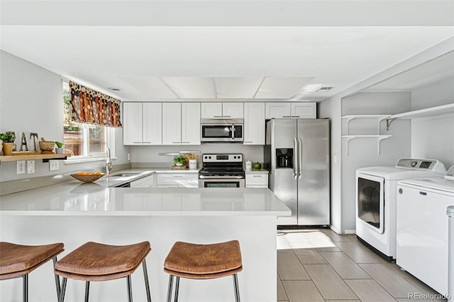 kitchen featuring stainless steel appliances, a breakfast bar, washer and clothes dryer, kitchen peninsula, and white cabinetry