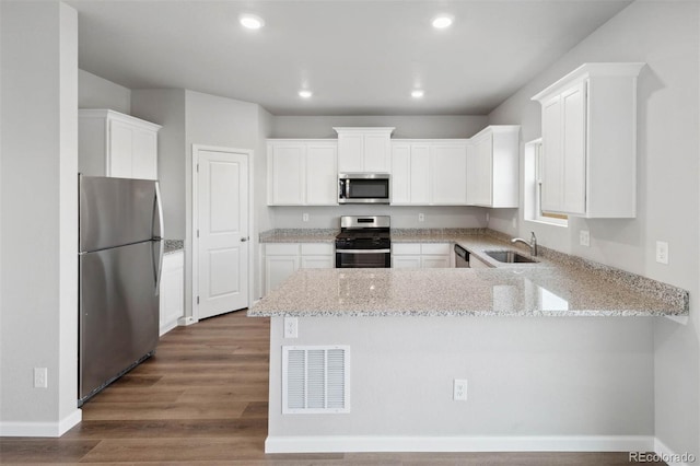 kitchen featuring wood finished floors, visible vents, a peninsula, a sink, and stainless steel appliances