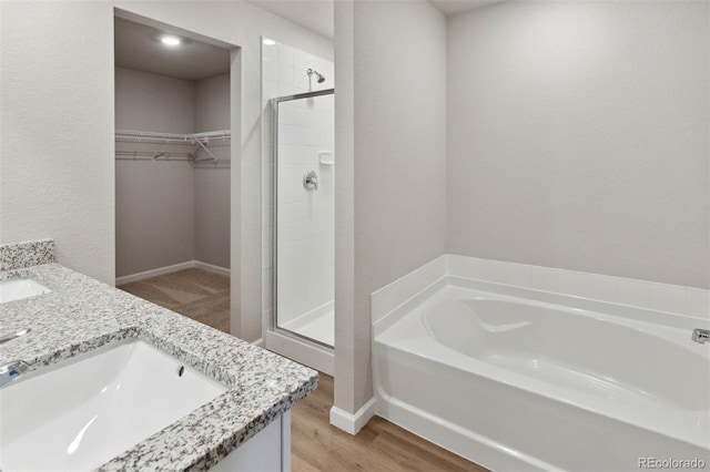 bathroom featuring wood finished floors, a sink, a shower stall, a spacious closet, and a bath