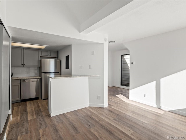 kitchen with light stone countertops, dark wood-type flooring, tasteful backsplash, gray cabinets, and appliances with stainless steel finishes