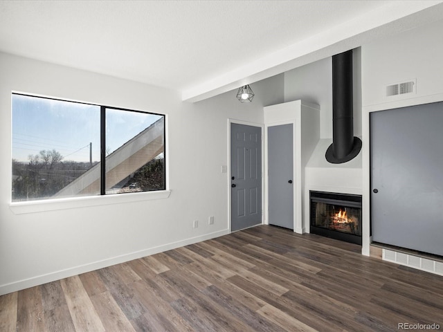 unfurnished living room with a fireplace, beam ceiling, and dark wood-type flooring