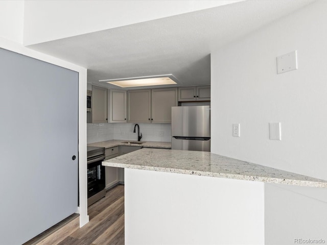 kitchen featuring backsplash, sink, hardwood / wood-style flooring, appliances with stainless steel finishes, and kitchen peninsula