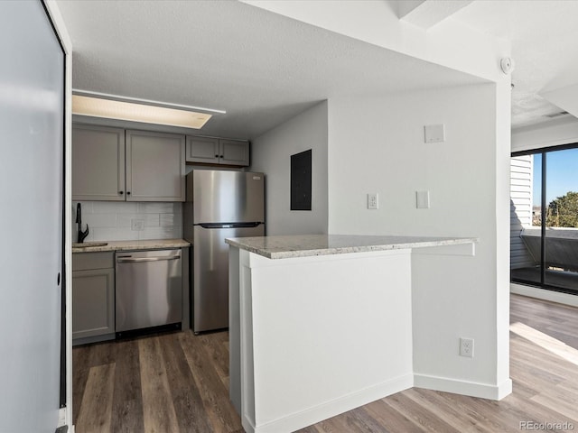 kitchen with decorative backsplash, dark hardwood / wood-style flooring, kitchen peninsula, and stainless steel appliances