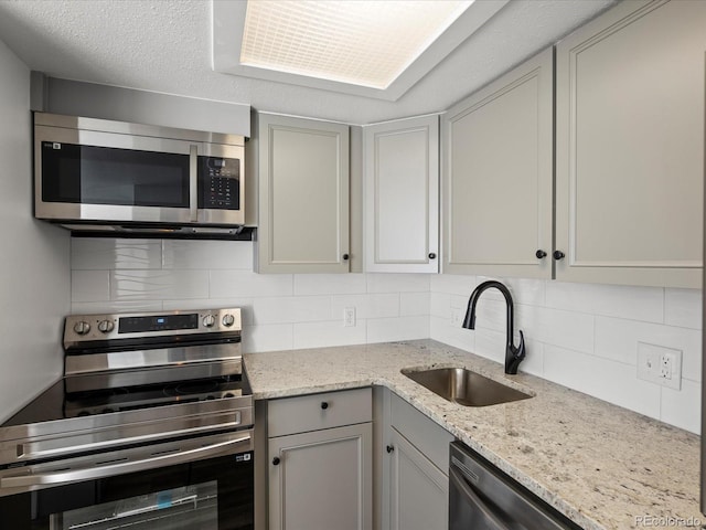 kitchen featuring decorative backsplash, stainless steel appliances, light stone counters, and sink