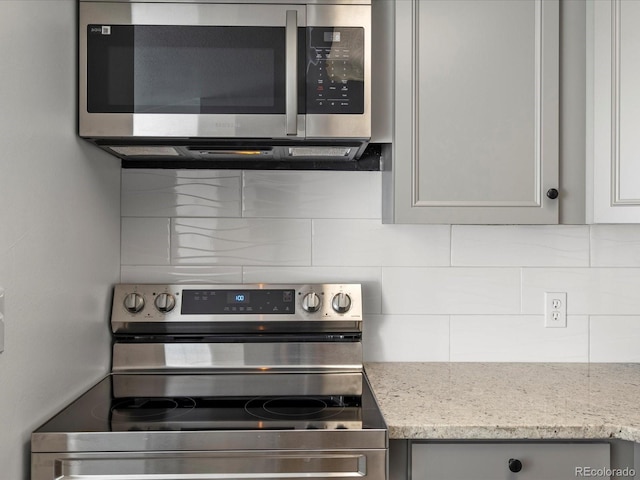 kitchen featuring light stone countertops, stainless steel appliances, gray cabinets, and tasteful backsplash