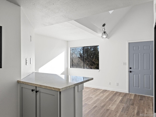 kitchen featuring gray cabinetry, a textured ceiling, vaulted ceiling, light hardwood / wood-style floors, and hanging light fixtures