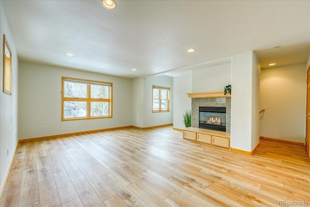 unfurnished living room with recessed lighting, baseboards, light wood-style floors, and a glass covered fireplace