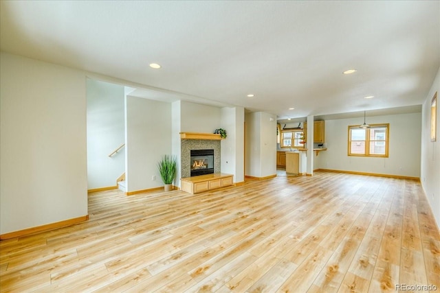 unfurnished living room featuring a tiled fireplace, recessed lighting, stairway, light wood-style floors, and baseboards