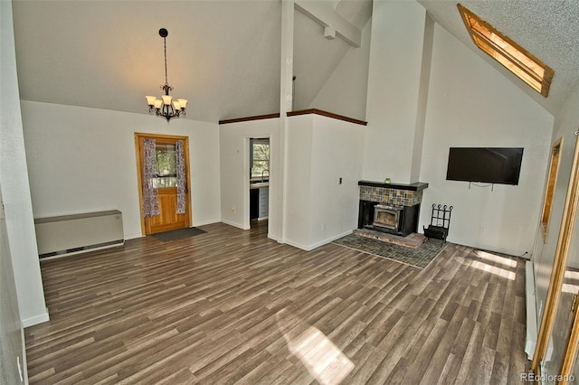 unfurnished living room featuring a wood stove, dark hardwood / wood-style flooring, high vaulted ceiling, and a notable chandelier