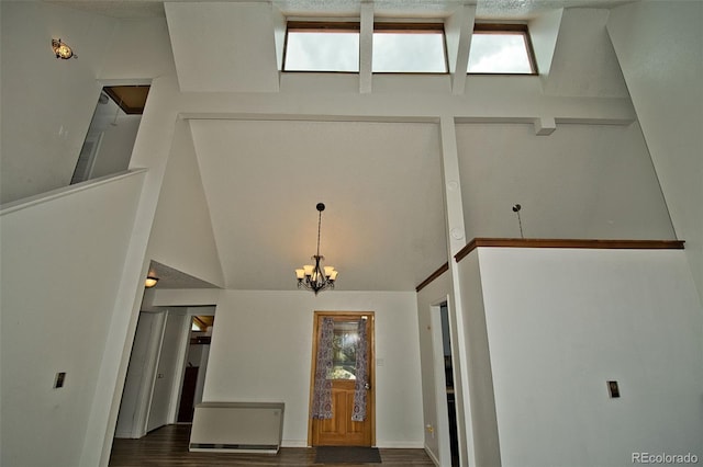 foyer entrance with dark wood-type flooring, high vaulted ceiling, and a notable chandelier