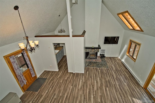 living room with dark hardwood / wood-style flooring, a baseboard radiator, an inviting chandelier, high vaulted ceiling, and a wood stove