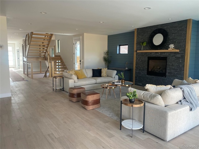 living area with recessed lighting, stairway, a large fireplace, and light wood-style flooring